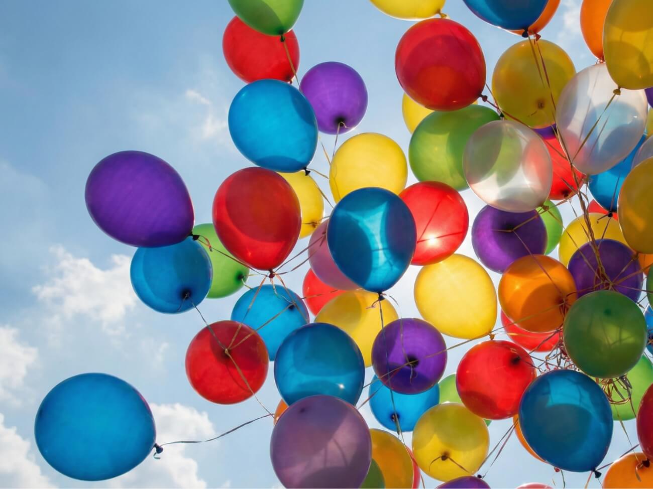Blauer Himmel und im Vordergrund sind viele bunte Luftballons zu sehen.