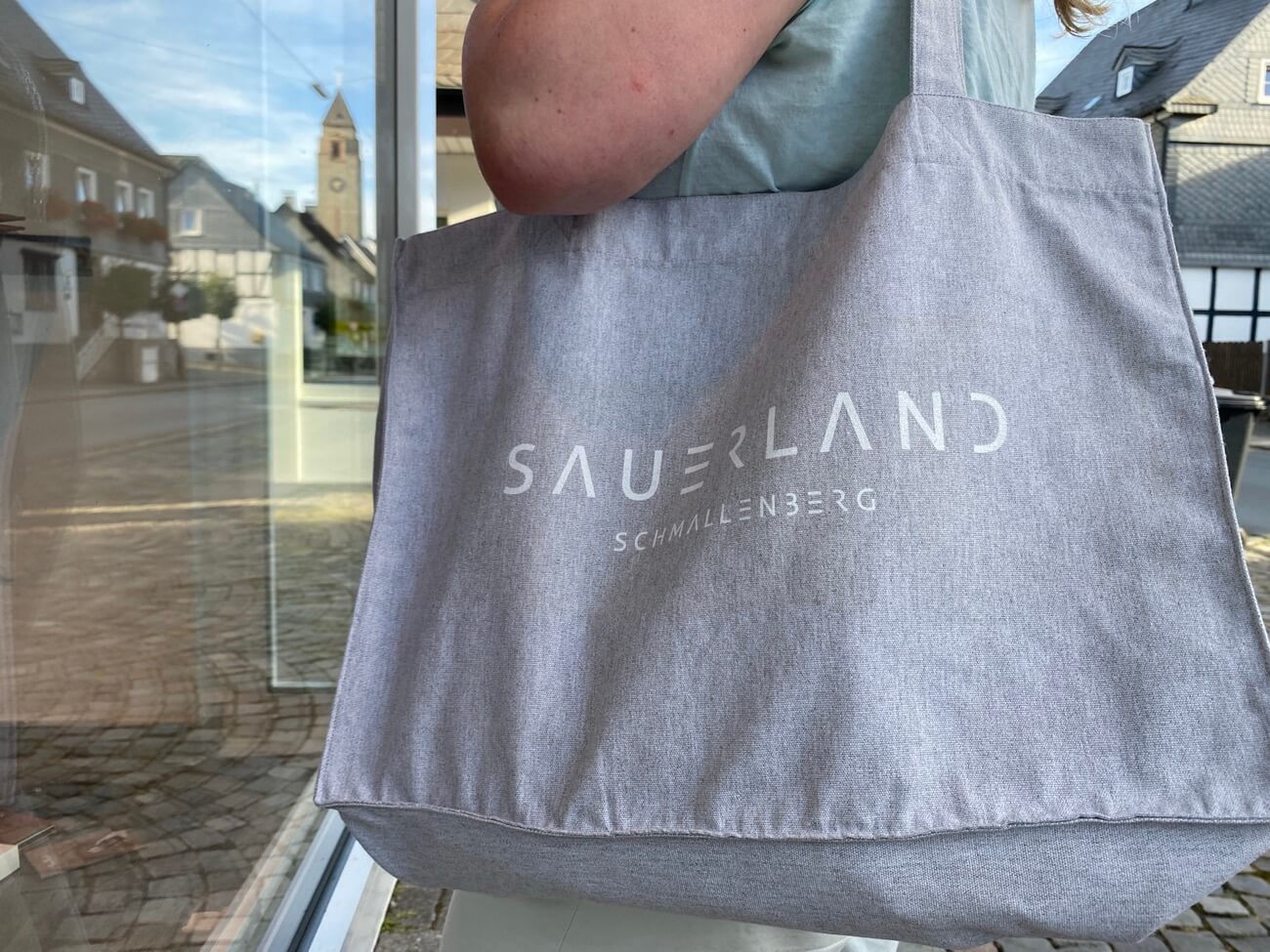 Eine Frau steht vor einem Schaufenster mit einer newSAUERLAND Shopping Tasche.