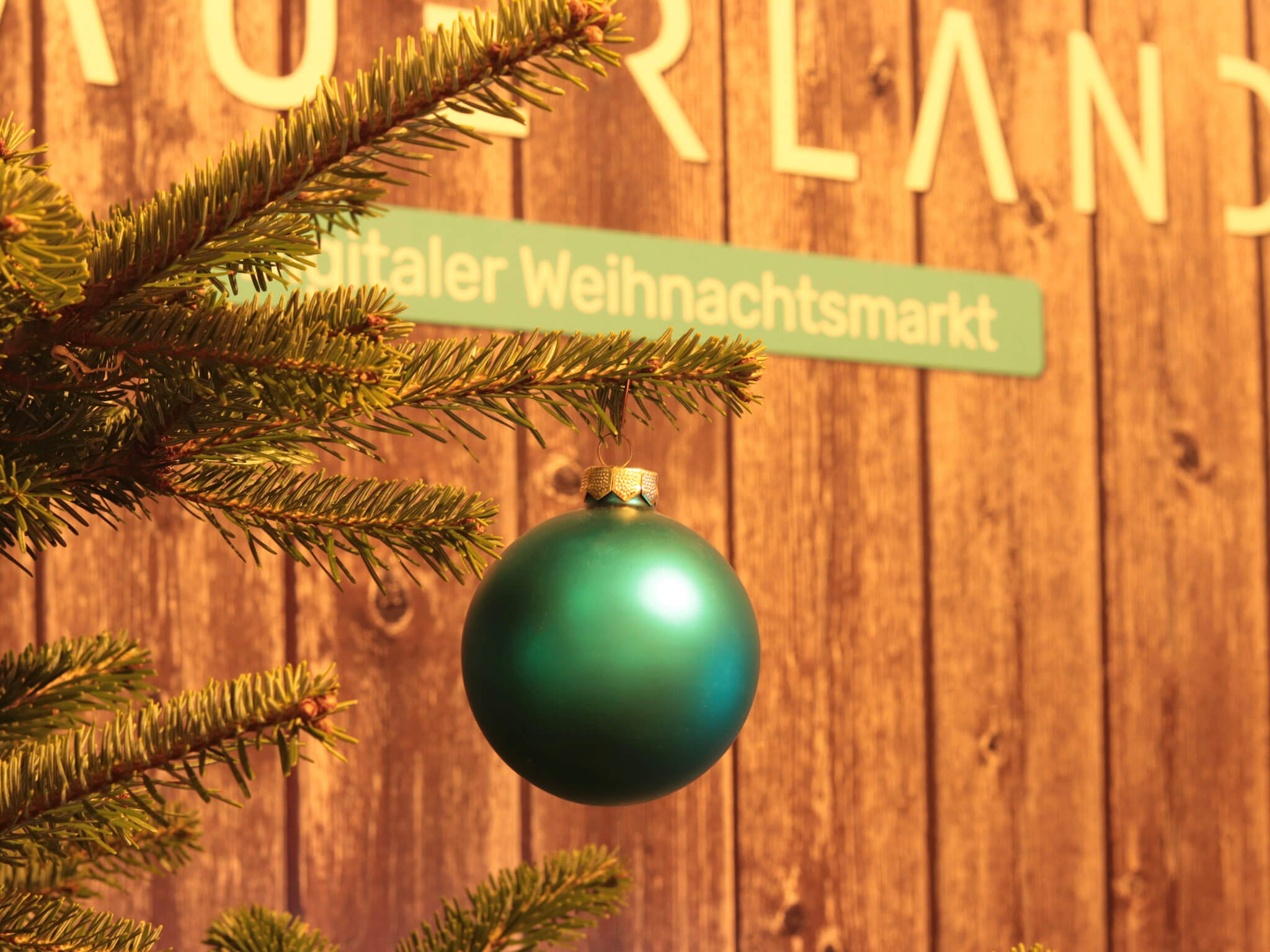 Eine blaue Weihnachtsbaumkugel hängt an einem Tannenzweig vor einem Hintergrund aus Holz