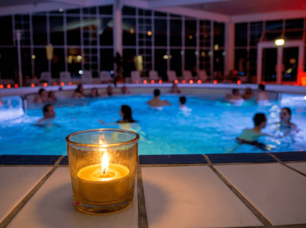 Eine Kerze im Vordergrund und ein schön beleuchtetes Schwimmbad im Hintergrund