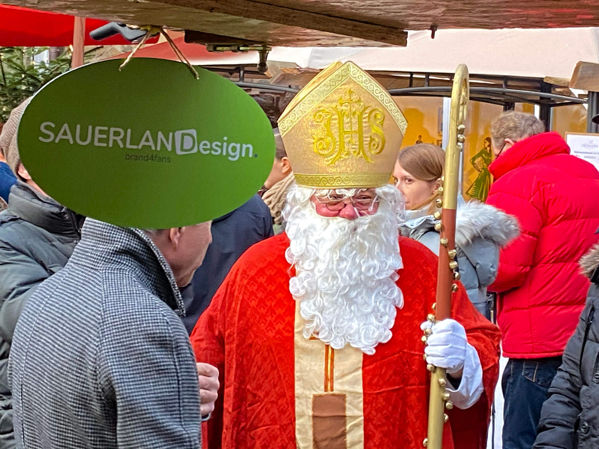 Ein als Nikolaus kostümierter Mann geht über einen gut besuchtem Weihnahctsmarkt zwischen den Besuchern entlang