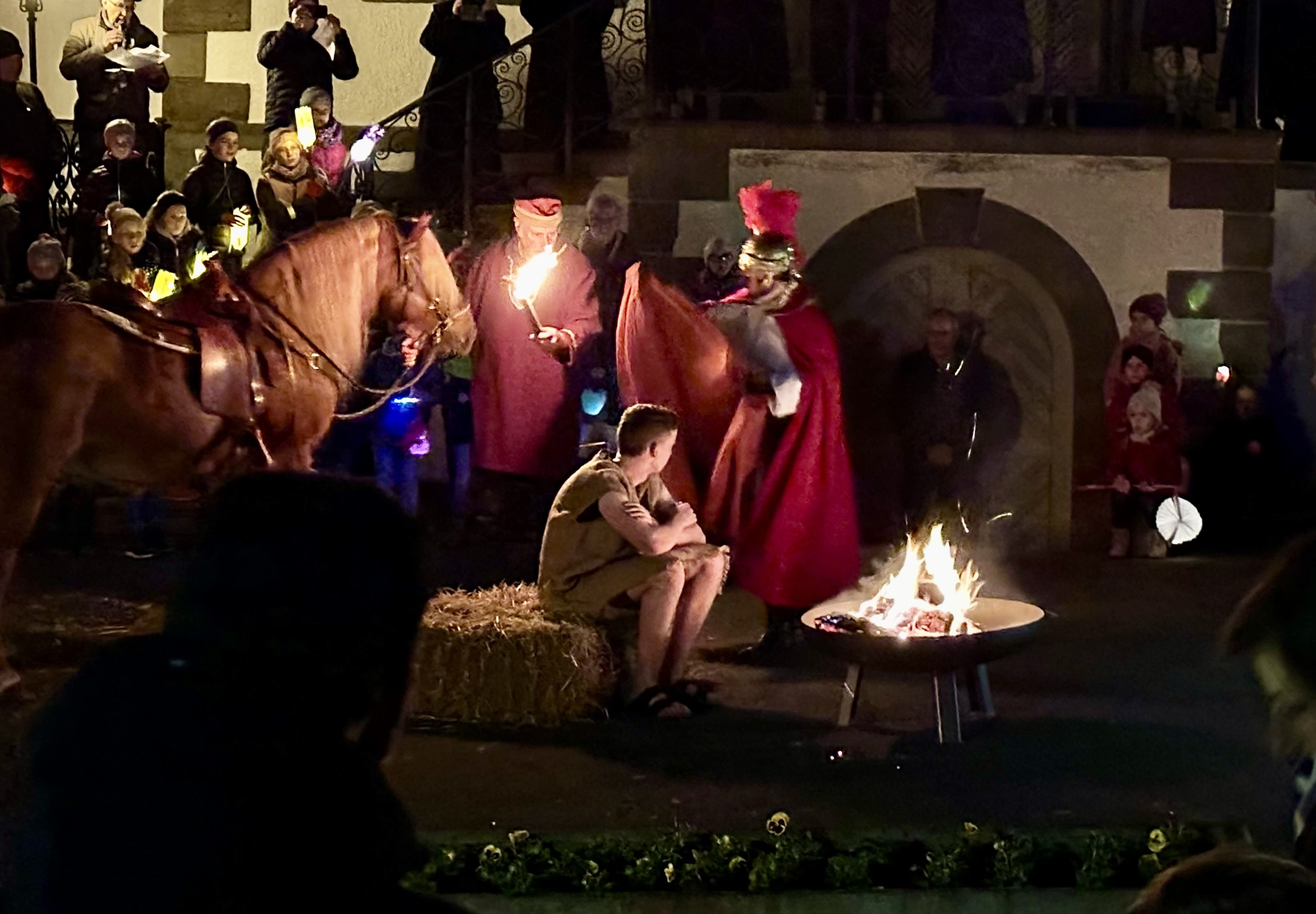 Szenen von einem St.Martin Schauspiel. Ein Bettler sitzt in Lumpen vor einem Lagerfeuer und ein Pferd ist im Hintergrund