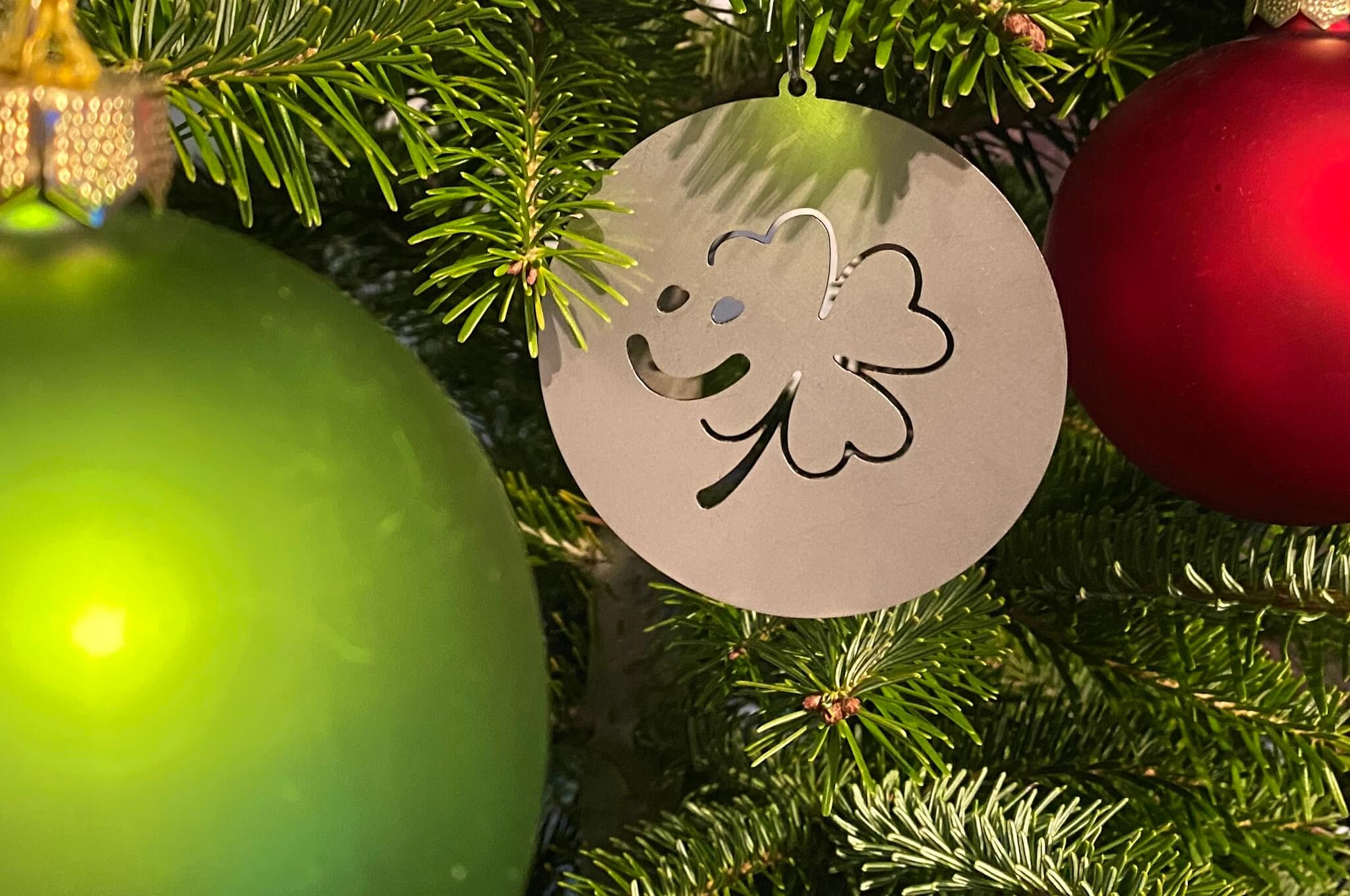 Nahaufnahme eines geschmückten Weihnachtsbaums, im Vordergrund sind 3 Bunte Weihnachtsbaumkugeln